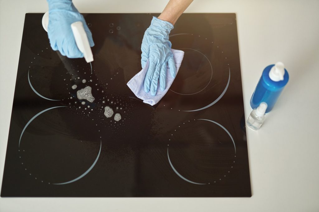 Top view of female hands in rubber gloves cleaning cooktop in the kitchen using cloth and detergent